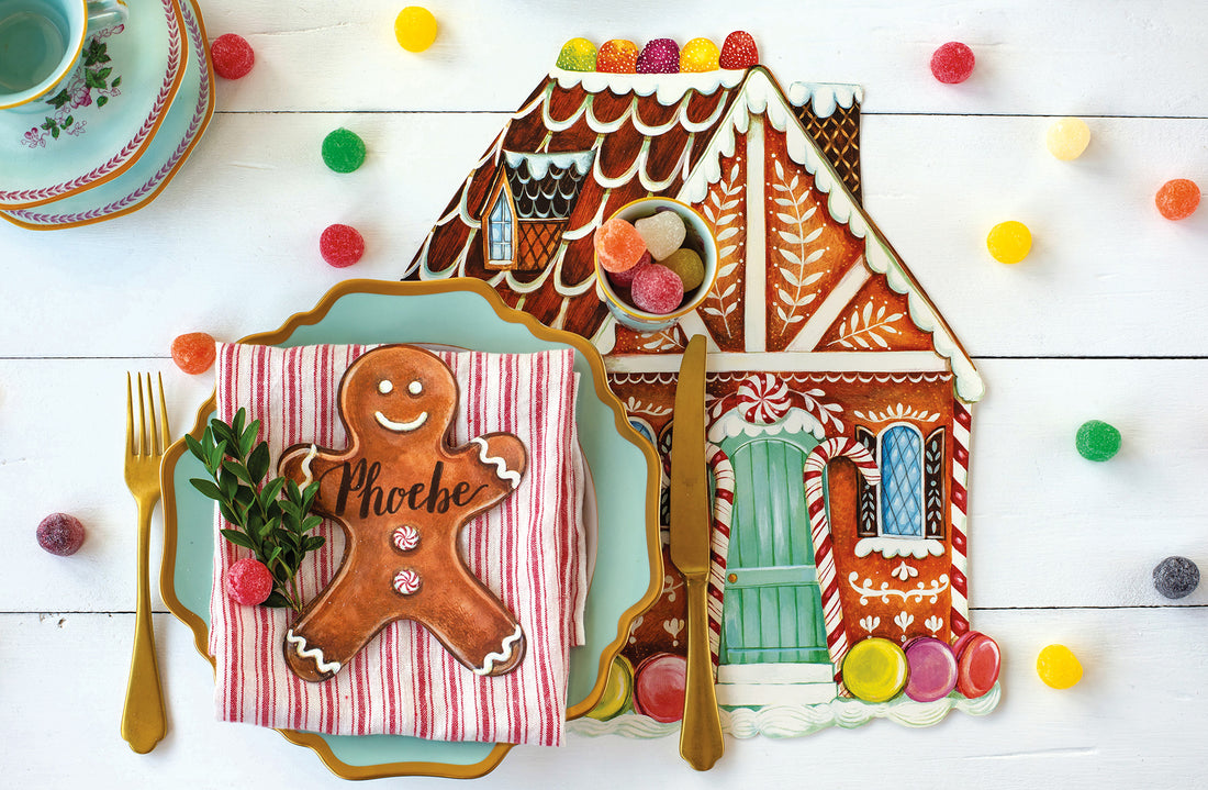 An illustrated die-cut gingerbread house in rich brown with white icing, decorated with colorful candies and a seafoam green door.