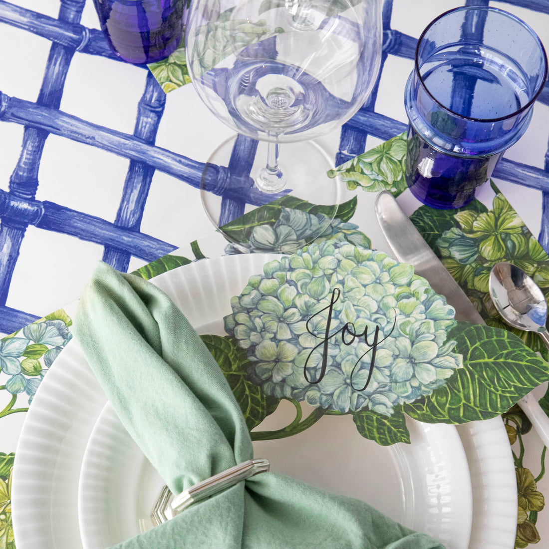 A Hydrangea Table Accent with &quot;Joy&quot; written on it in beautiful script resting on the plate of an elegant place setting.