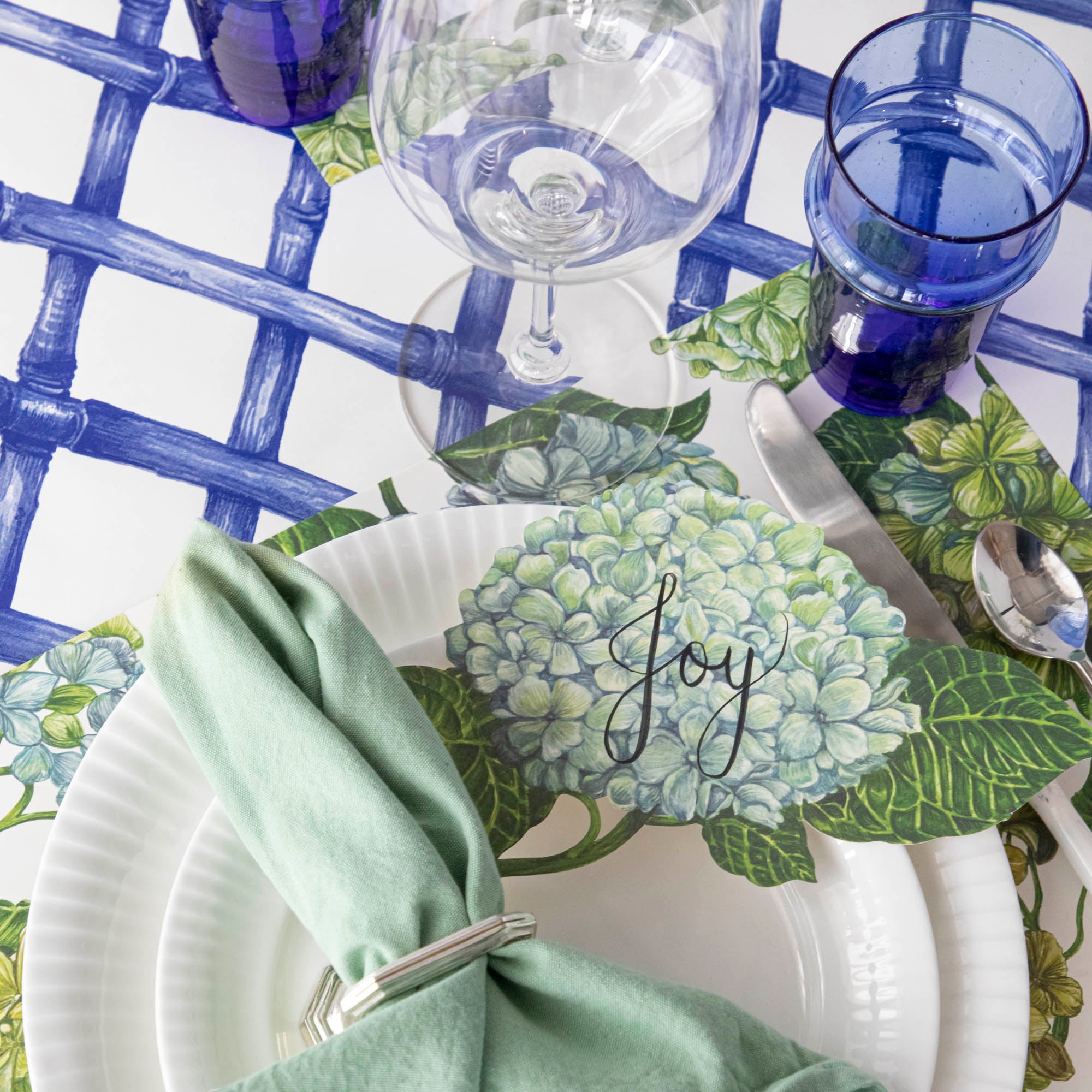 A Hydrangea Table Accent with "Joy" written on it in beautiful script resting on the plate of an elegant place setting.