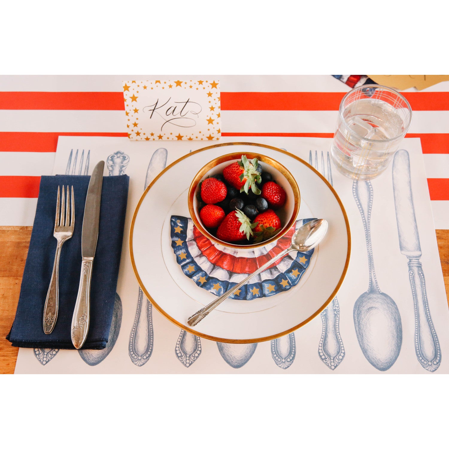 An elegant patriotic place setting featuring a Shining Star Place Card labeled &quot;Kat&quot; standing behind the plate.