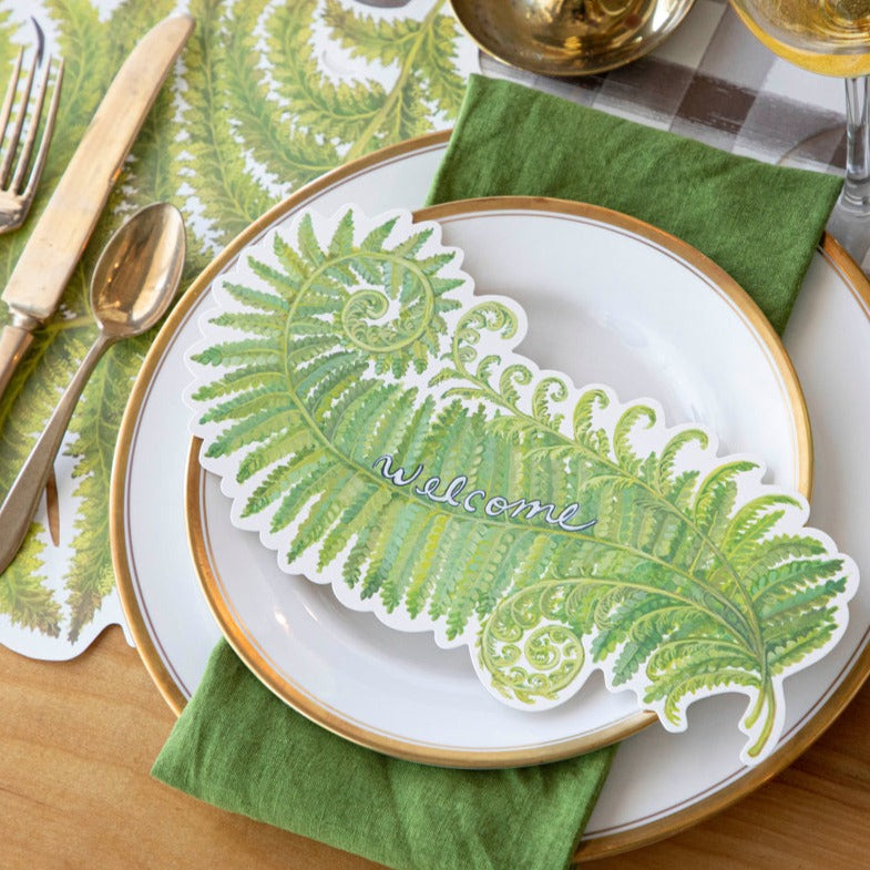 A Fern Fronds Table Accent with "Welcome" written on it resting on the plate of an elegant place setting.
