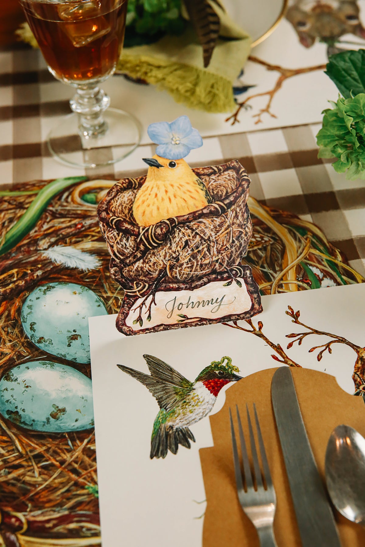 An elegant, avian place setting featuring a Welcome Warbler Place Card labeled "Johnny" standing at the edge of the placemat.