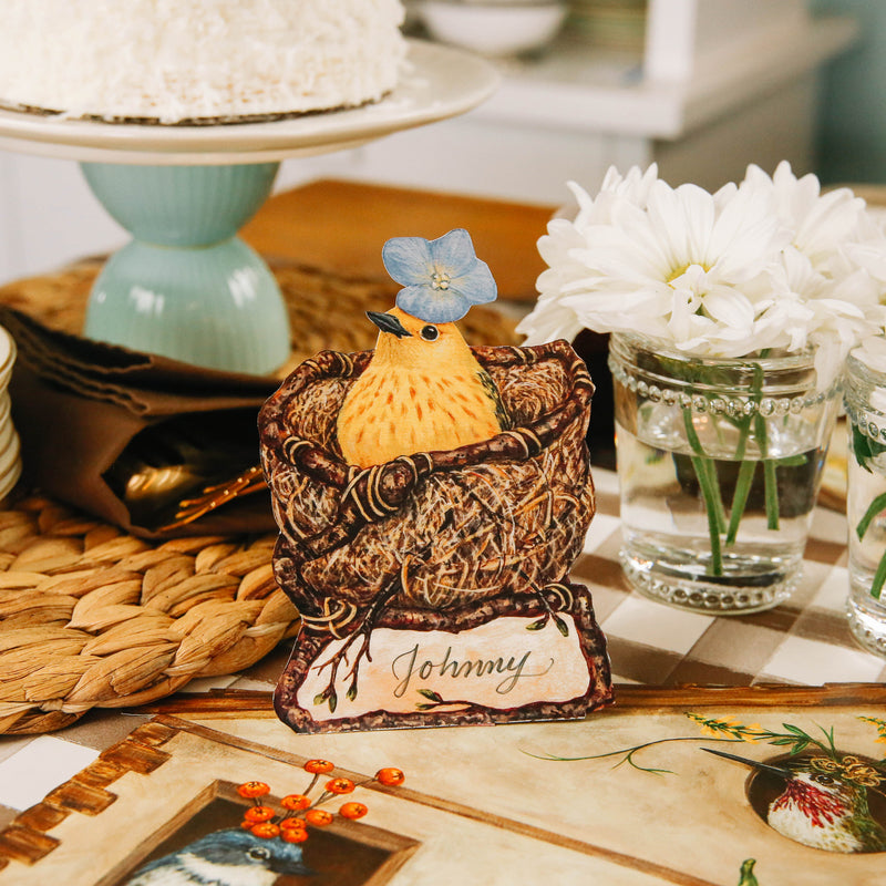 Close-up of a Welcome Warbler Place Card labeled "Johnny" standing on an elegant table setting.