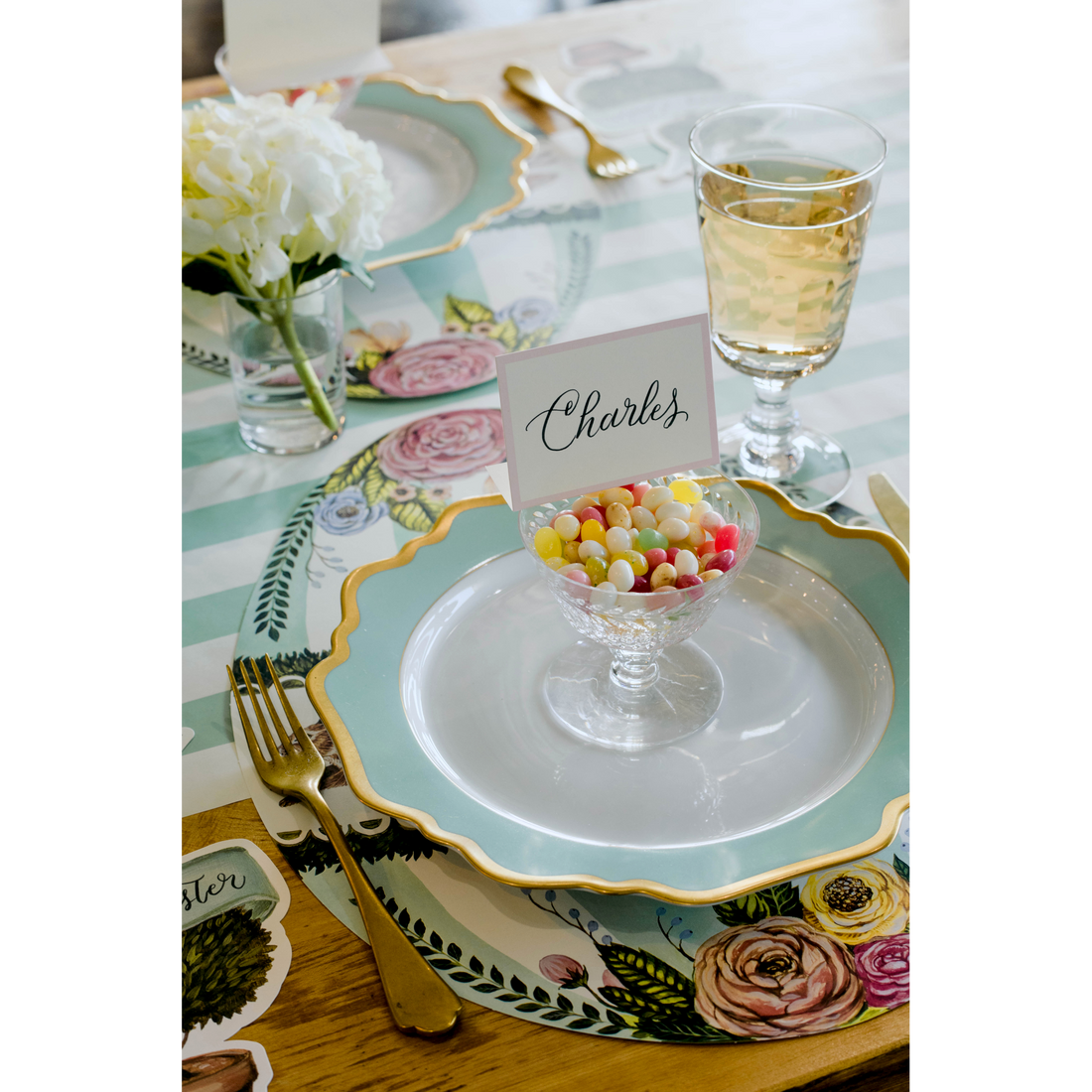An elegant Easter place setting featuring a Pink Frame Place Card labeled &quot;Charles&quot; perched on top of a bowl of candy on a plate.