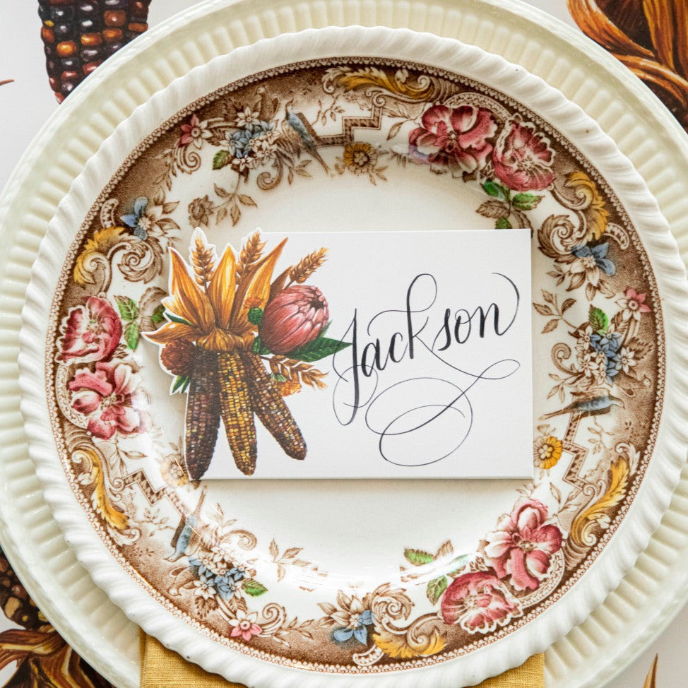 Close-up of an elegant Thanksgiving place setting featuring a Gathering Place Card labeled &quot;Jackson&quot; centered on the plate, from above.