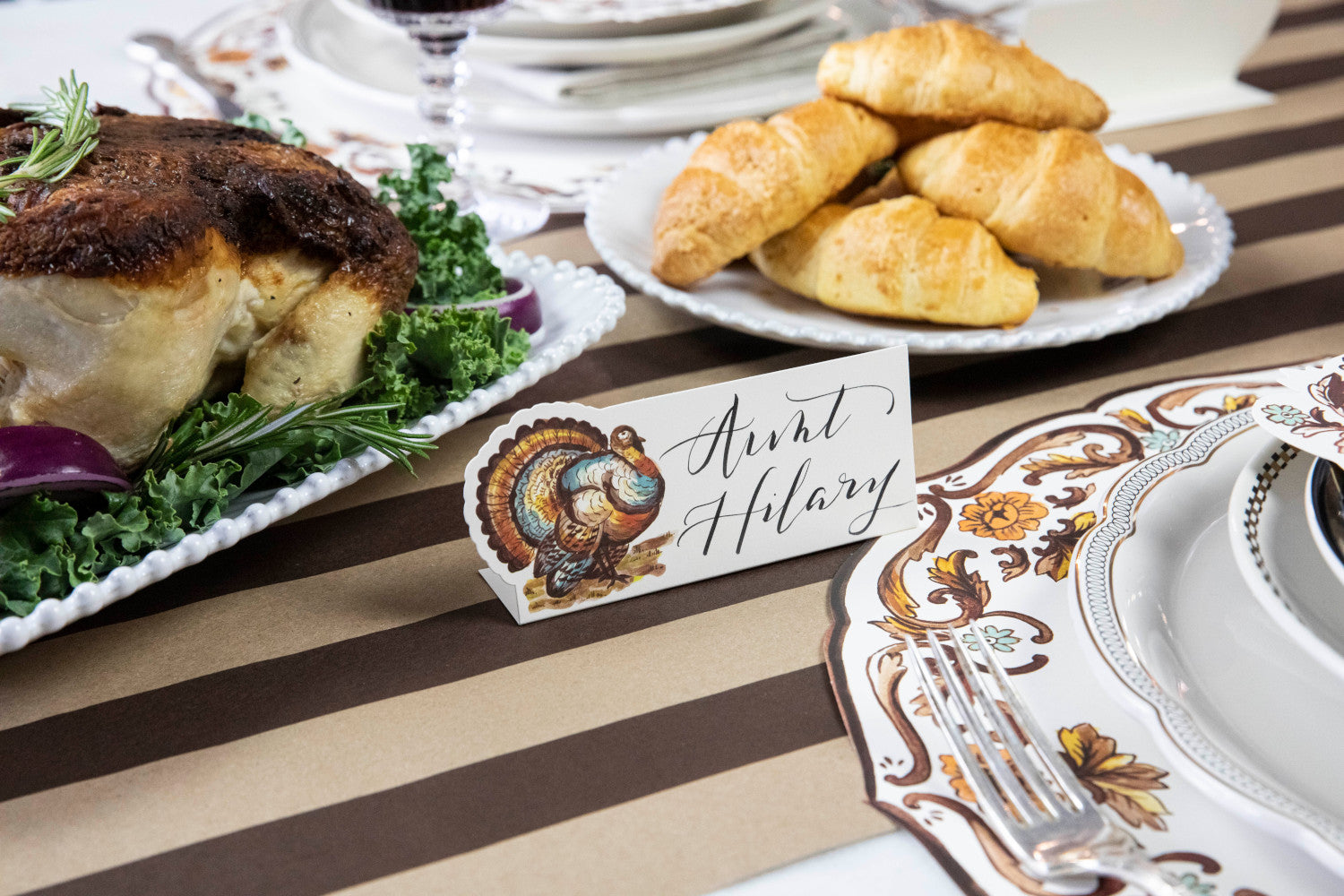 Close-up of a Thanksgiving Turkey Place Card labeled "Aunt Hilary" standing next to the plate of an elegant place setting.