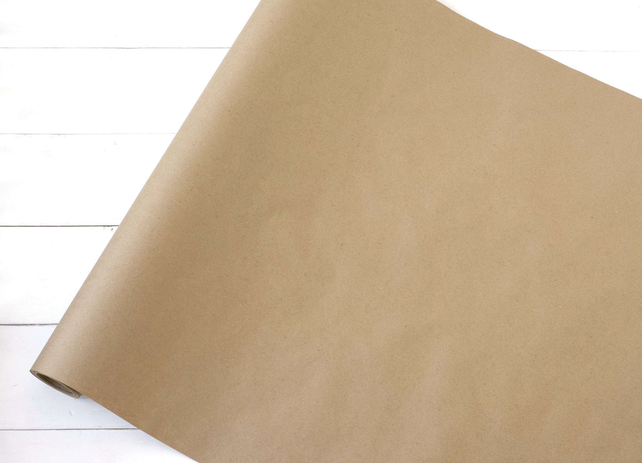 A roll of Basic Kraft Runner by Hester & Cook, perfect for gift wrapping or as a table runner, rests gracefully on a rustic wooden floor.