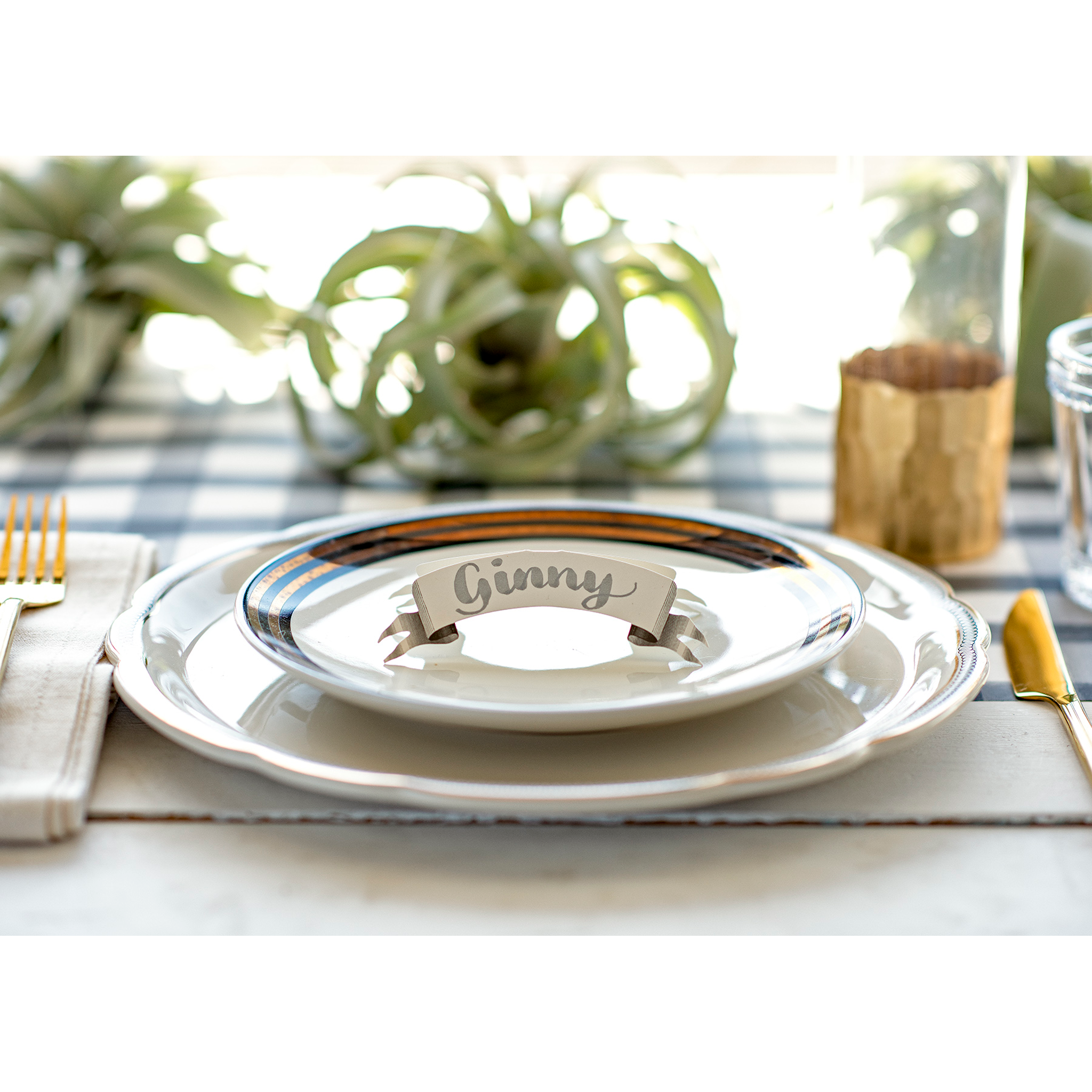 An elegant place setting featuring a Banner Place Card reading "Ginny" standing on the plate.