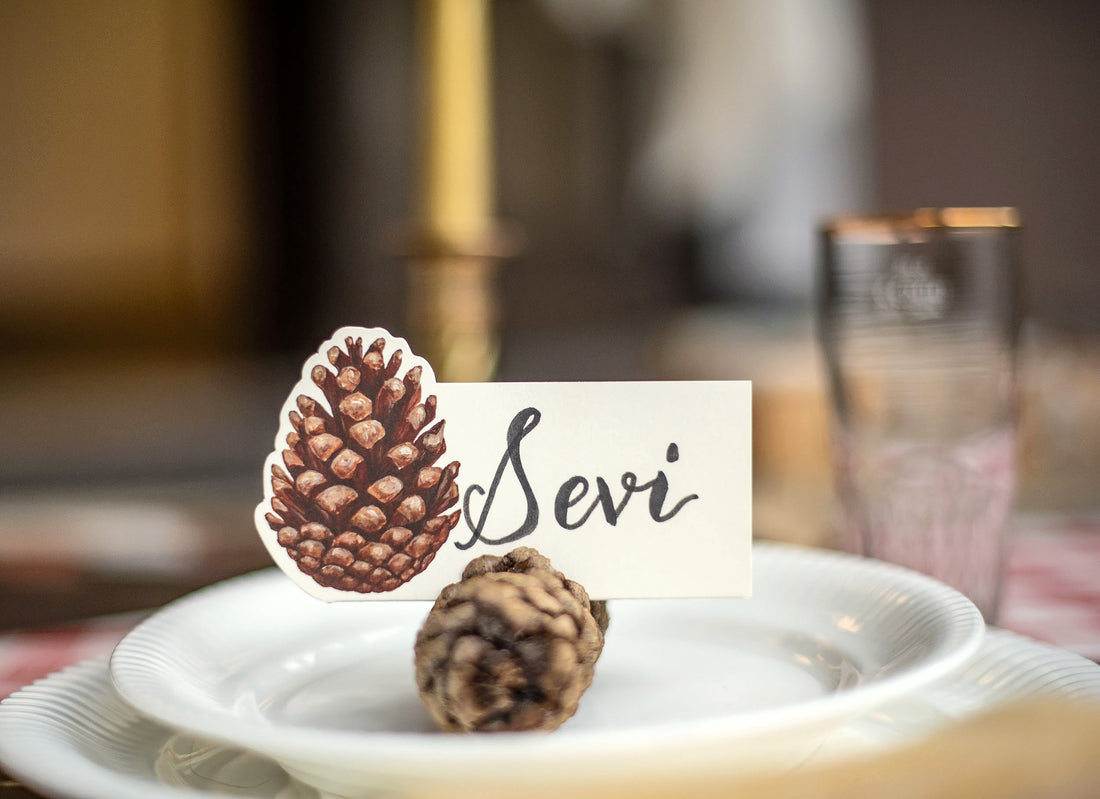An elegant place setting featuring a Pinecone Place Card being held up by a real pinecone on a plate.