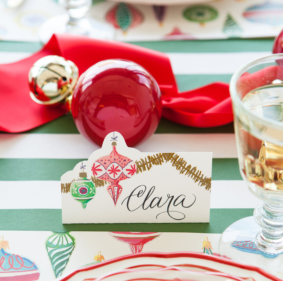 Close-up of an Ornaments Place Card labeled &quot;Clara&quot; in beautiful script, standing behind the plate of a festive holiday place setting.