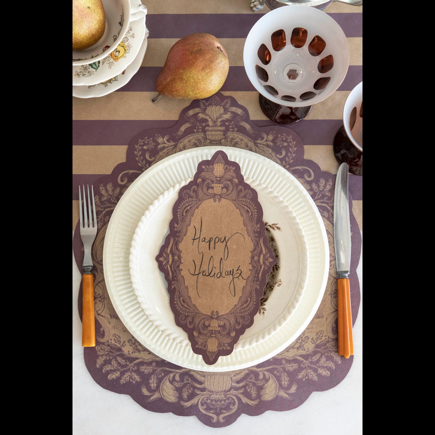 Top-down view of a rustic place setting featuring a Fable Toile Table Accent with "Happy Holidays" written on it resting on the plate.