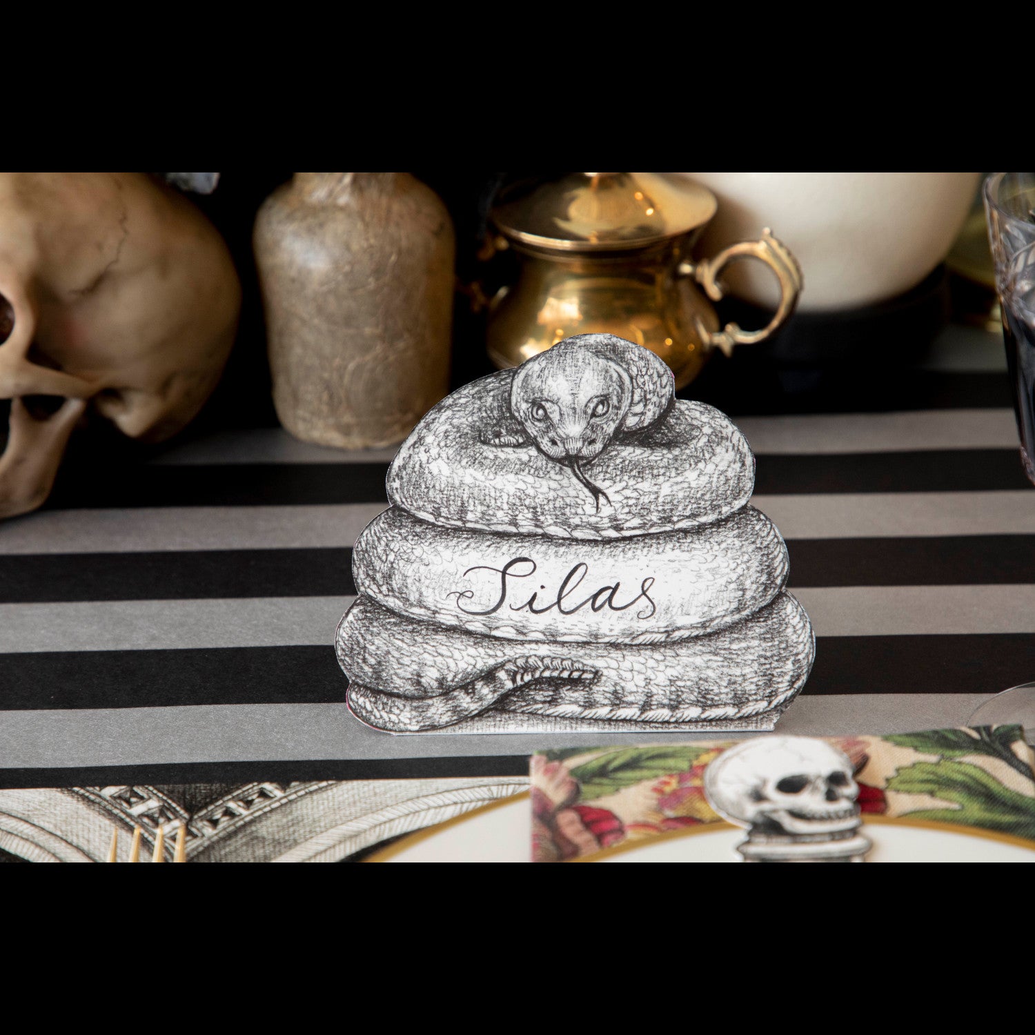 A Coiled Snake Place Card reading "Silas" standing on a spooky Halloween-themed tablescape.