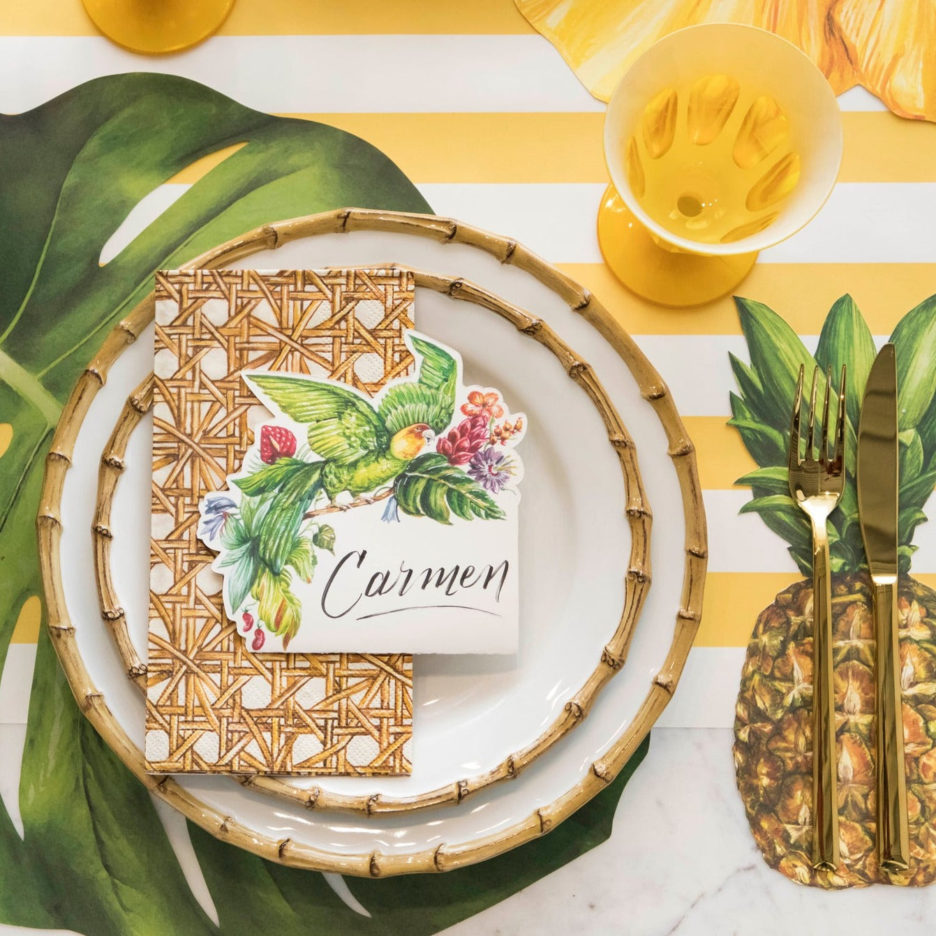 Top-down view of a vibrant tropical-themed place setting featuring a Parrot Place Card labeled &quot;Carmen&quot; laying flat on the plate.