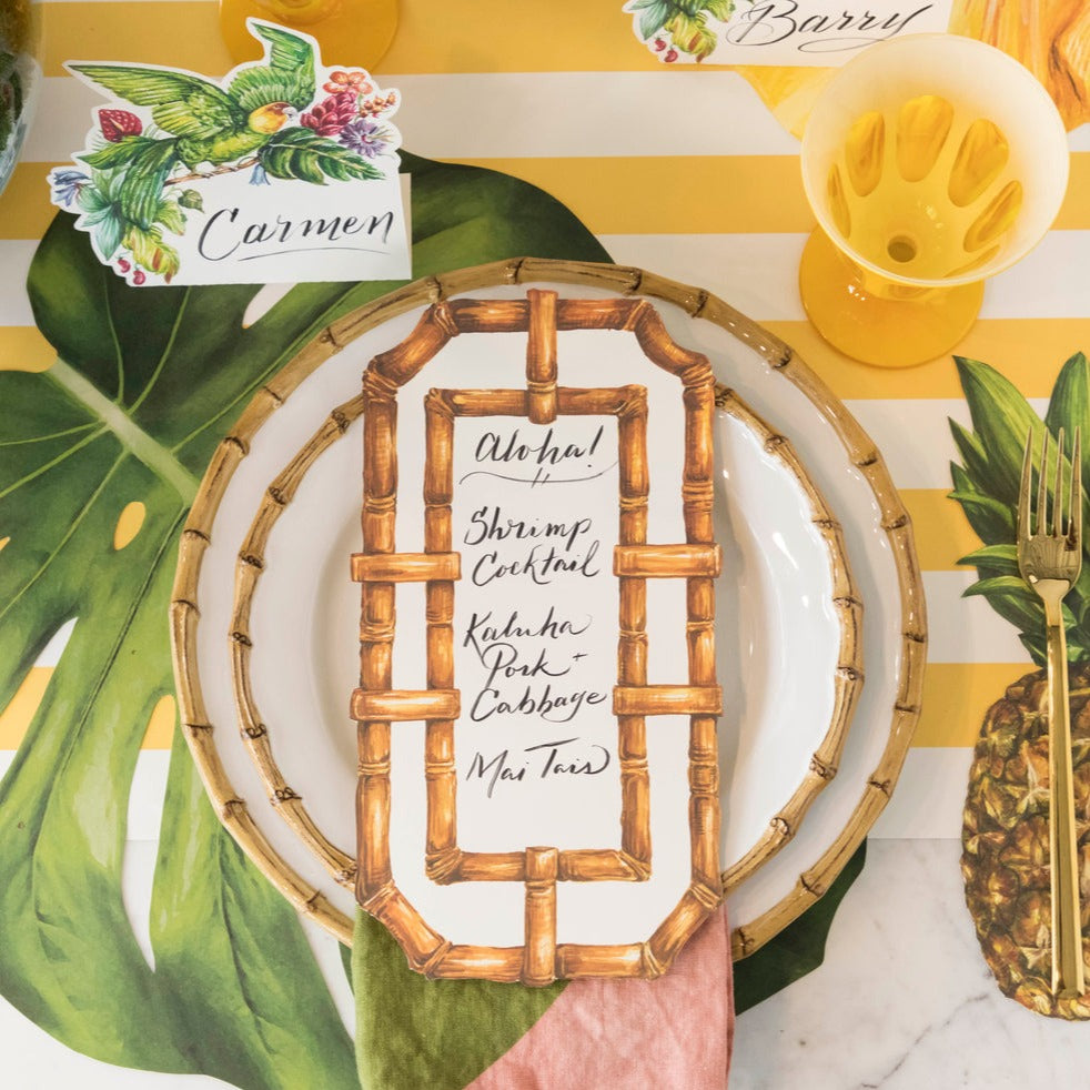 A tropical-themed place setting featuring a Bamboo Table Card with a menu written on it resting on the plate, from above.