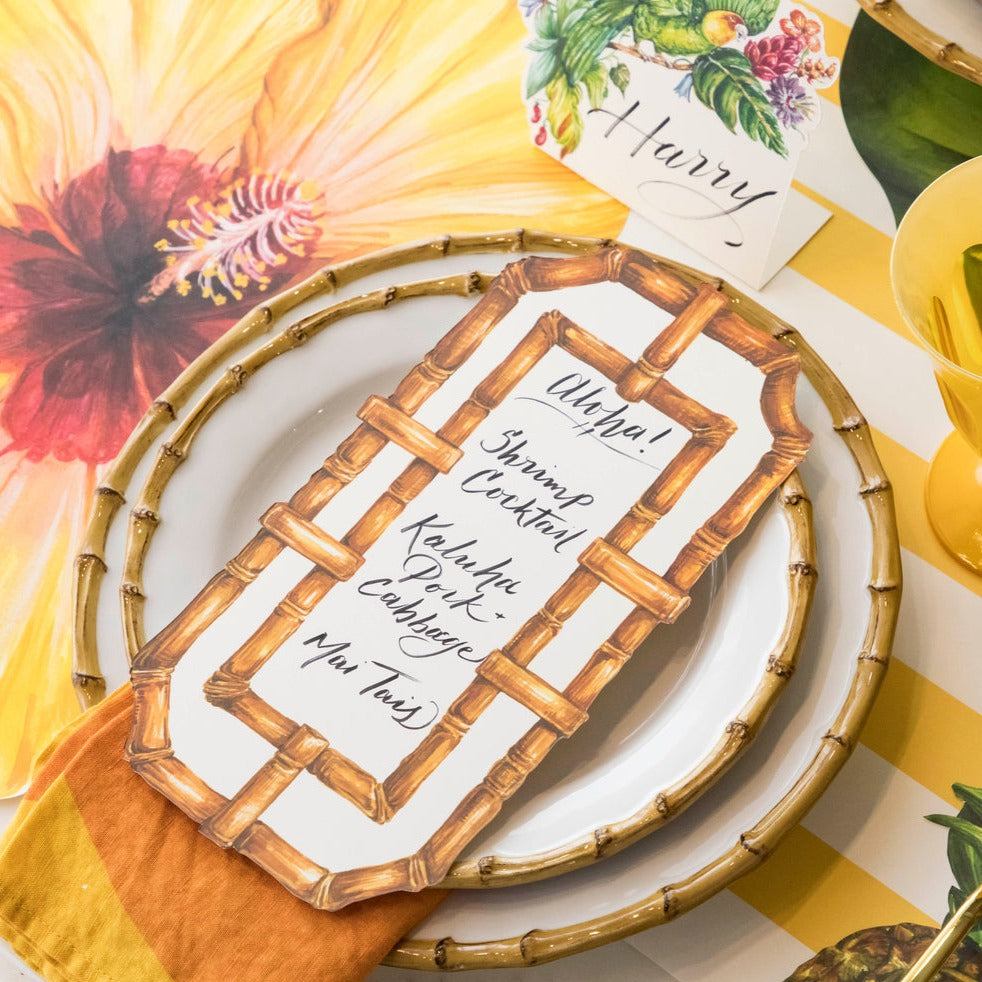 A tropical-themed place setting featuring a Bamboo Table Card with a menu written on it resting on the plate.
