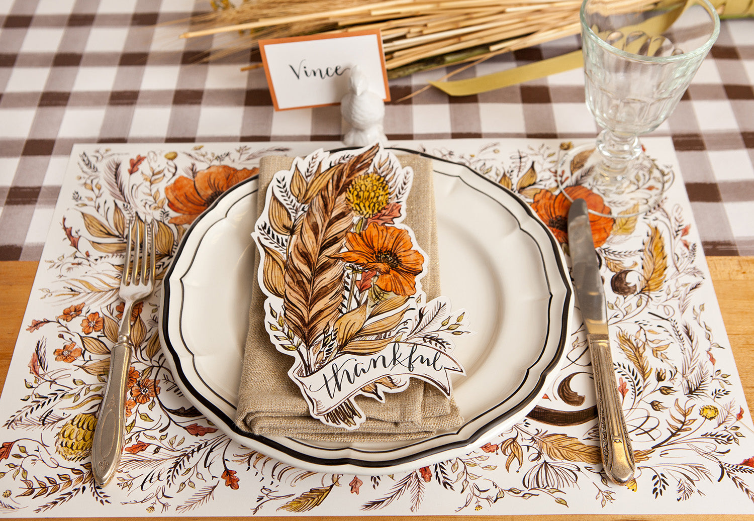 An elegant Thanksgiving place setting featuring a Feather Table Accent resting on the plate with "Thankful" written on it in beautiful script.