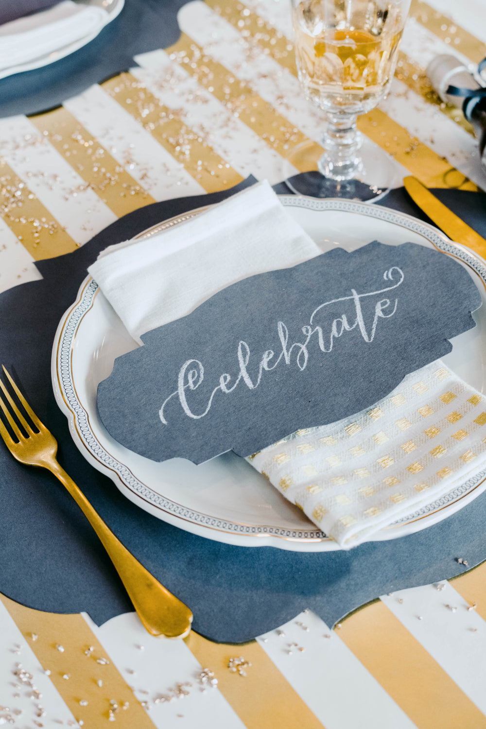 A festive place setting featuring a Gray Frame Table Accent resting on the plate with "Celebrate" hand-written in white script.