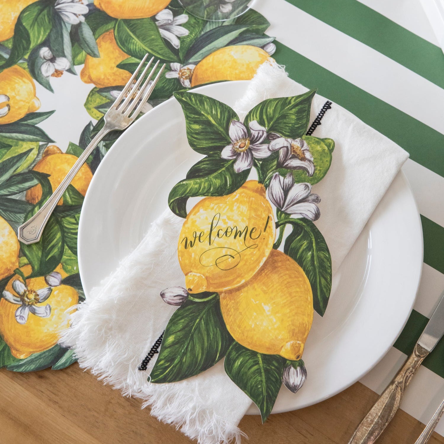 A vibrant citrus-themed place setting featuring a Lemon Table Accent with "Welcome!" written on it resting on the table.