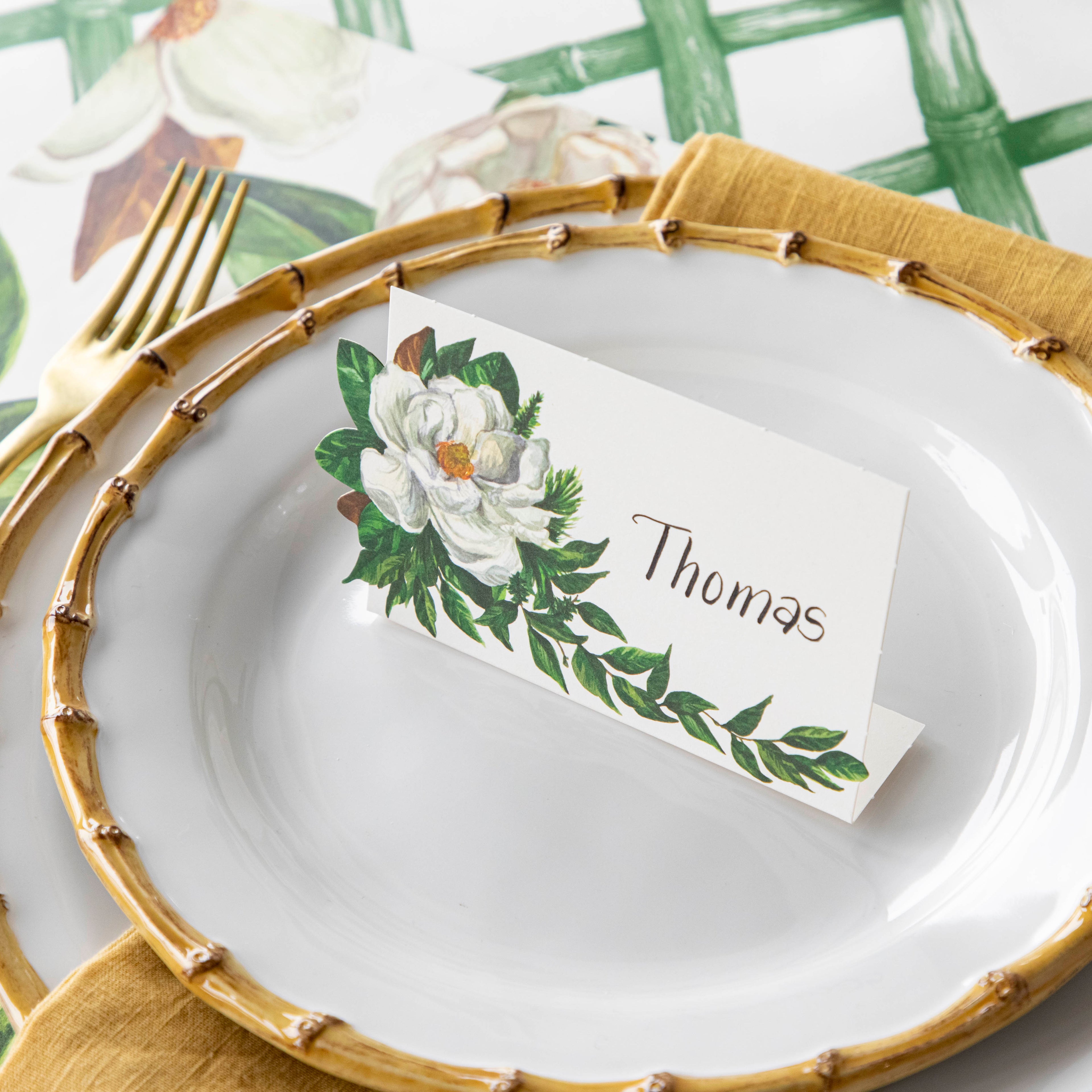 Close-up of a Magnolia Place Card labeled "Thomas" standing on the plate of an elegant place setting.