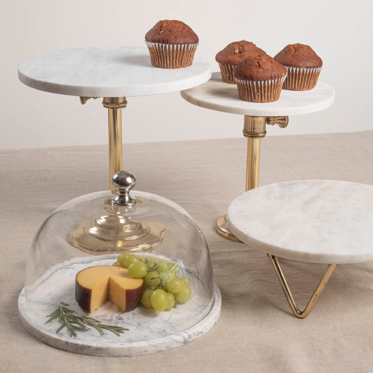 Two adjustable cake plates with marble tops and antique brass stands, one expanded to a larger size.