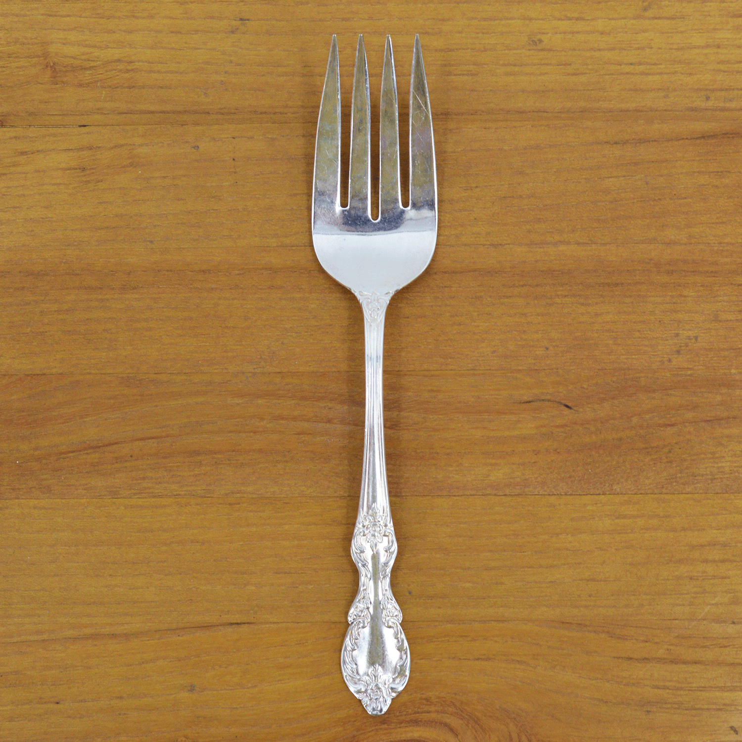 A Hester & Cook vintage silver-plate meat fork resting on a folded green napkin with pom-pom trim on a marble countertop.