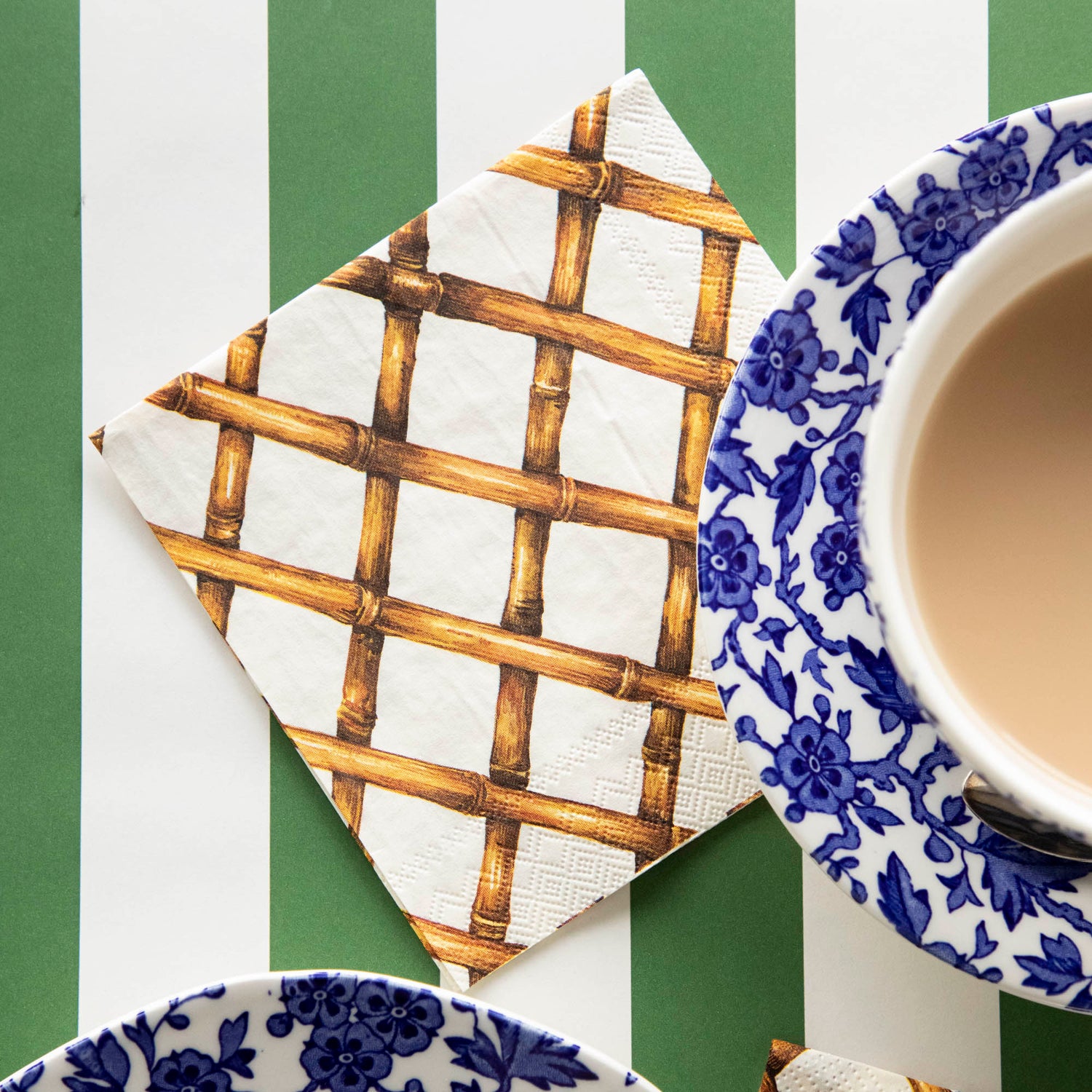 A Bamboo Lattice Cocktail Napkin on a striped table runner next to a cup of coffee.