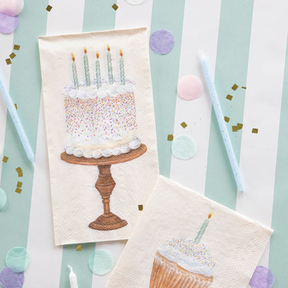 A Birthday Cake Guest Napkin next to a Cupcake Cocktail Napkin on a stripped table runner with confetti and birthday candles.