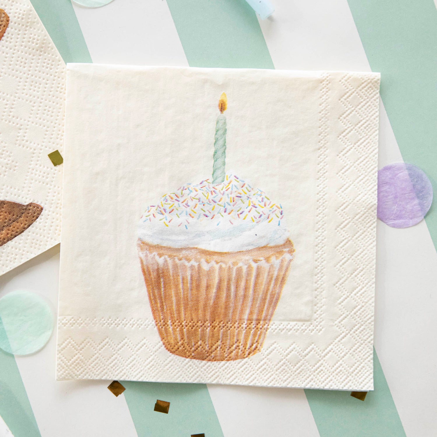 A Cupcake Cocktail Napkin on a striped table runner with confetti.