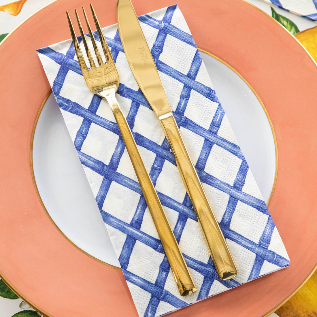 Close-up of a plate with a Blue Lattice Guest Napkin on it with a gold fork and knife on top.