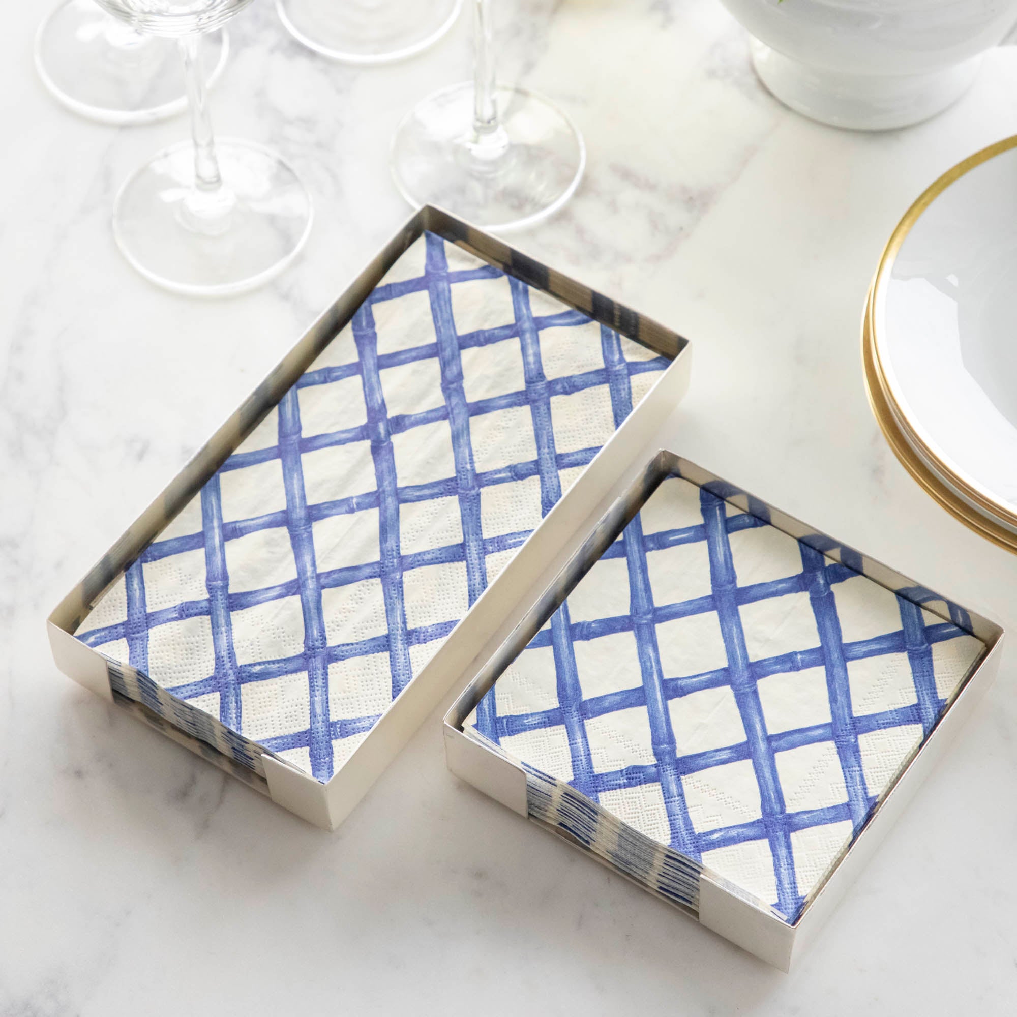 Two Silver Napkin Holders, guest-sized and cocktail-sized, containing blue and white napkins on a white table.