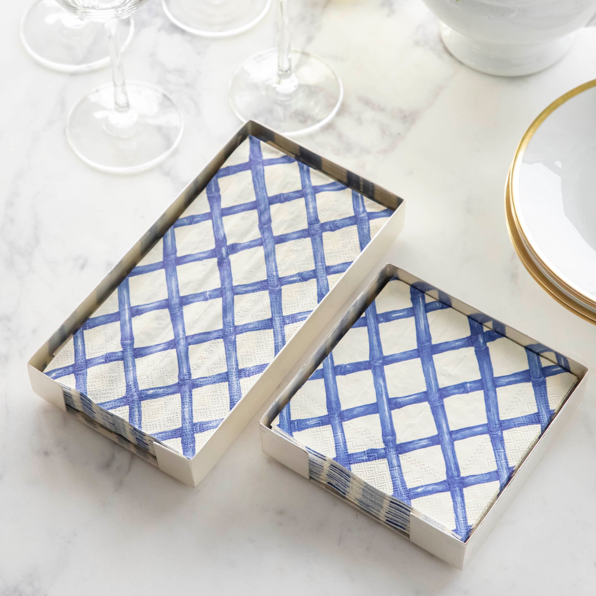 A stack of Blue Lattice Guest Napkins and a stack of Blue Lattice Cocktail Napkins in silver napkin holders on a marble table.