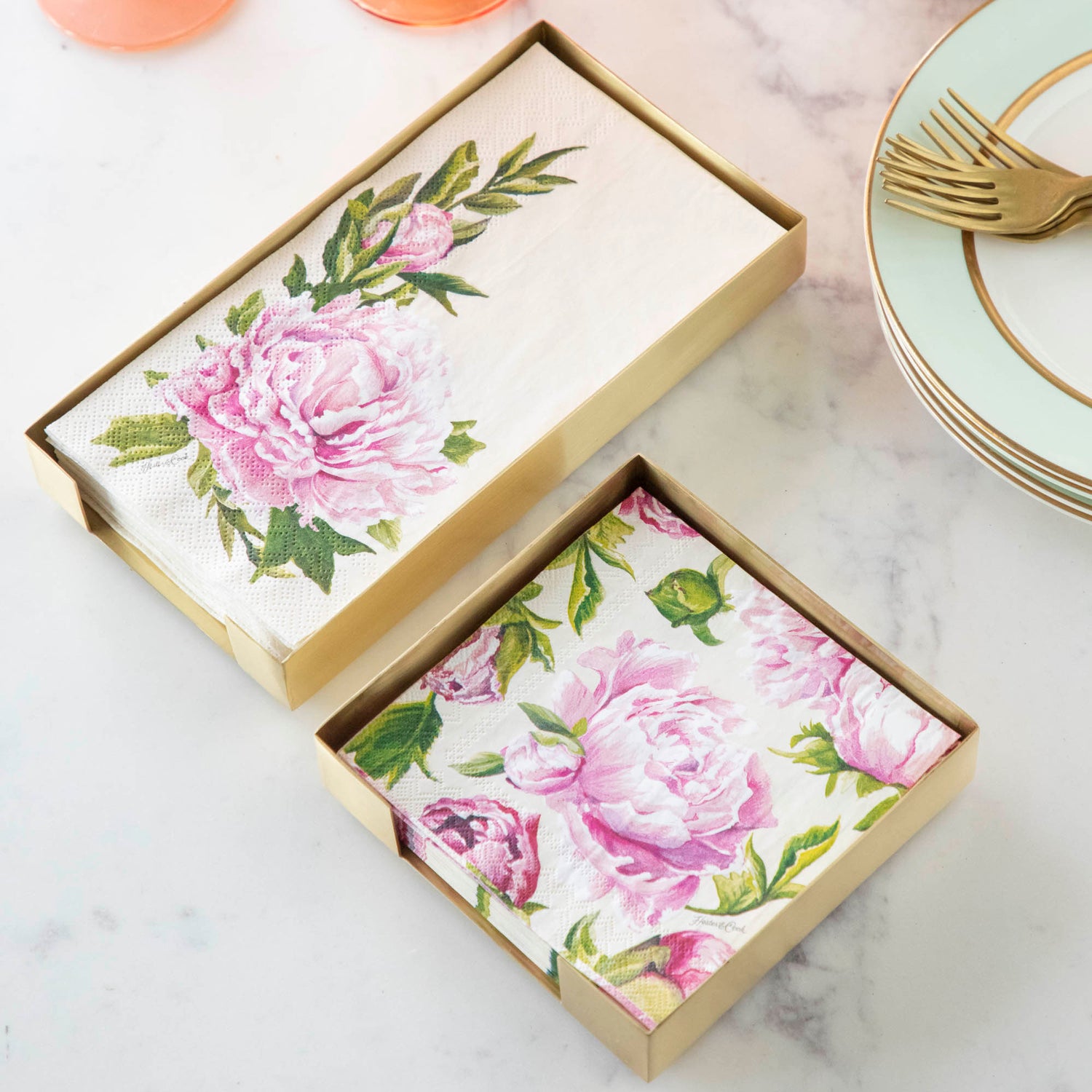 Two Brass Napkin Holders, guest-sized and cocktail-sized, containing pink floral napkins on a white table.