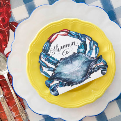 A nautical-themed place setting featuring a Crab Place Card laying flat on a yellow plate.