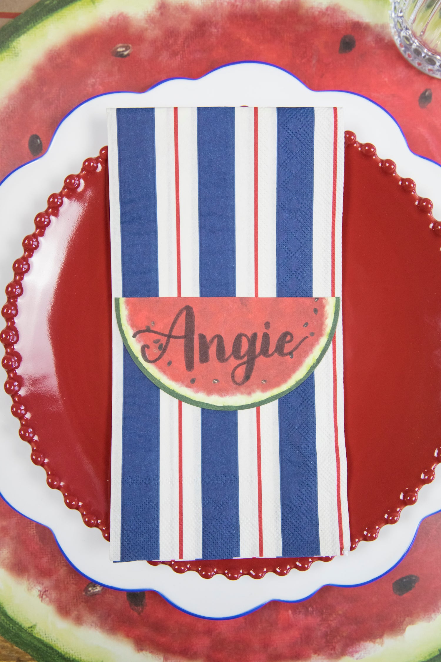 A Navy & Red Awning Stripe Guest Napkin centered on the plate of a summertime place setting.