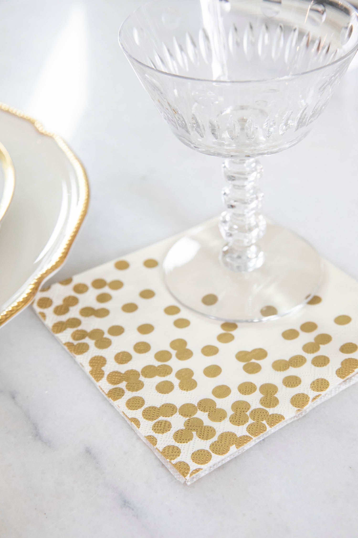 A Gold Confetti Cocktail Napkin under a water glass in an elegant place setting.
