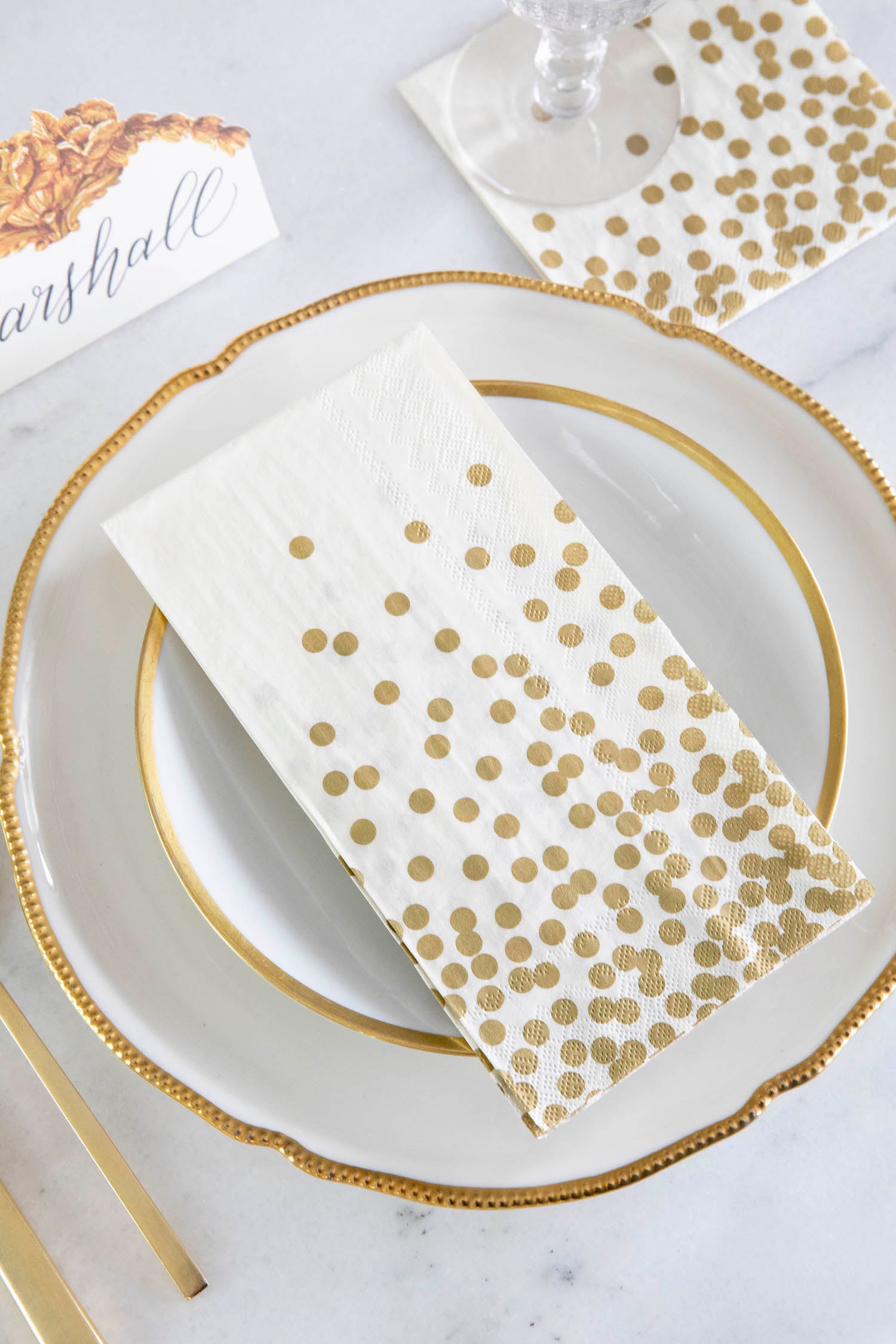 An elegant place setting featuring a Gold Confetti Guest Napkin on the plate, and a Gold Confetti Cocktail Napkin under the glass.