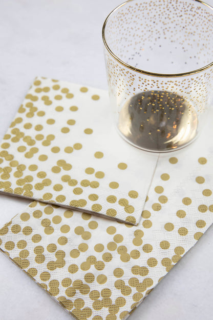Two Gold Confetti Napkins, one Guest and one Cocktail, together under a gold-accented glass on a white table.
