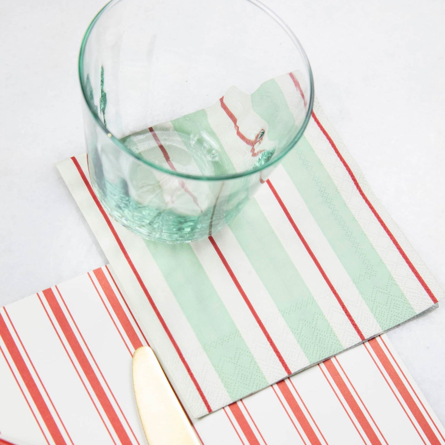 A Seafoam & Red Awning Stripe Cocktail Napkin in an elegant place setting.