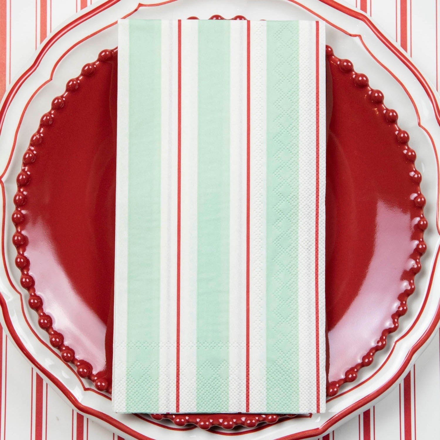 A Seafoam & Red Awning Stripe Guest Napkin centered on the plate of a place setting.