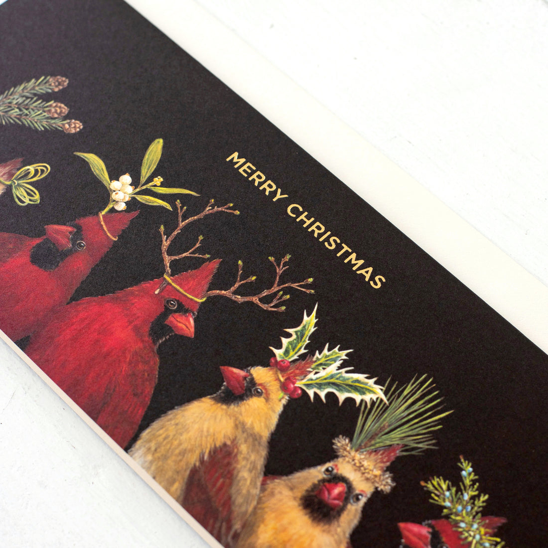 A festive Christmas card featuring a row of illustrated red cardinals with various plants and decorations on their heads, against a dark background, designed by Vicki Sawyer, with the greeting &quot;merry christmas&quot; is the Christmas Cardinals Boxed Set Cards from Hester &amp; Cook.