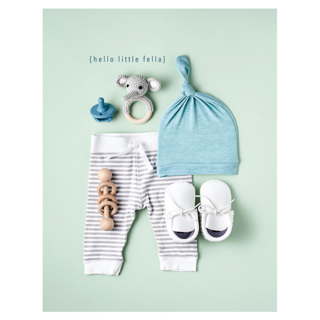 A photo of white and blue baby items including a cap, pants, shoes, a rattle and a pacifier on a light green background, with &quot;{hello little fella}&quot; printed in blue above the toys.