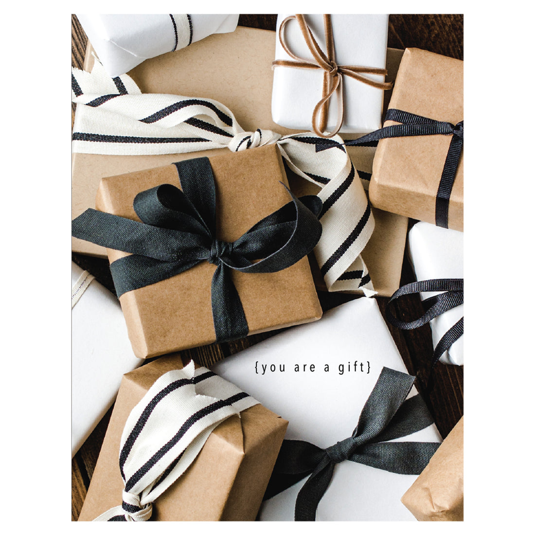 A close-up photo of a pile of simple wrapped gift boxes with ribbon in white, black and tan kraft paper, with &quot;{you are a gift}&quot; printed over a white gift.