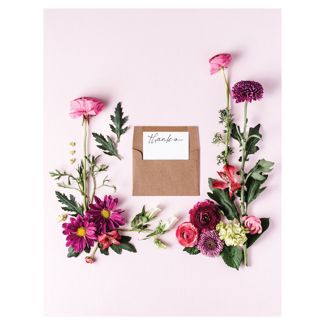 A photo of an open tan kraft paper envelope surrounded by various pink and purple flowers on a light pink background, with a hand-written note that says &quot;thanks&quot; peeking out of the envelope.