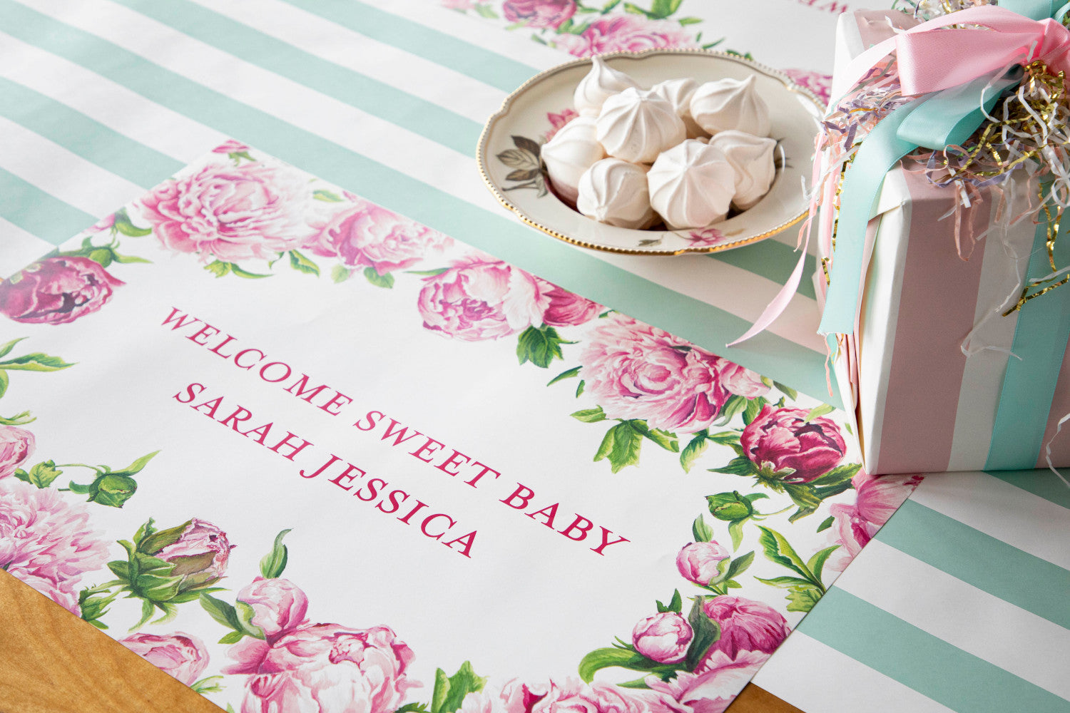The Peony Personalized Placemat on a baby-themed tablescape, with "WELCOME SWEET BABY SARAH JESSICA" printed in deep pink.