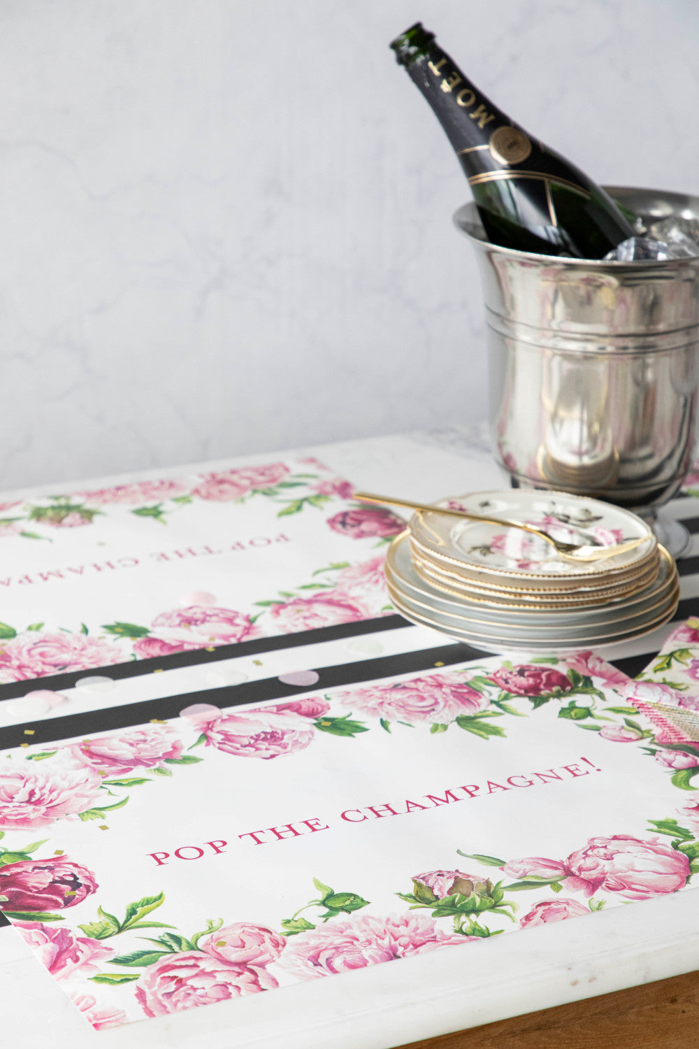 The Peony Personalized Placemat under a festive table setting, with &quot;POP THE CHAMPAGNE!&quot; printed in deep pink.
