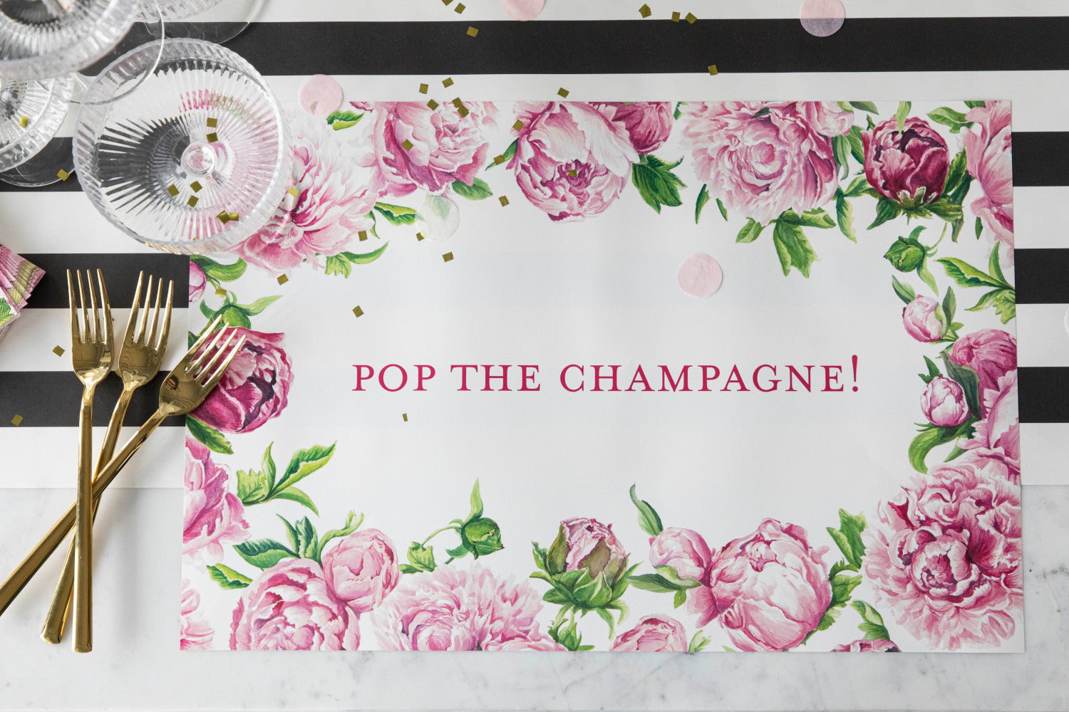 The Peony Personalized Placemat under a festive place setting, with &quot;POP THE CHAMPAGNE!&quot; printed in deep pink, from above.
