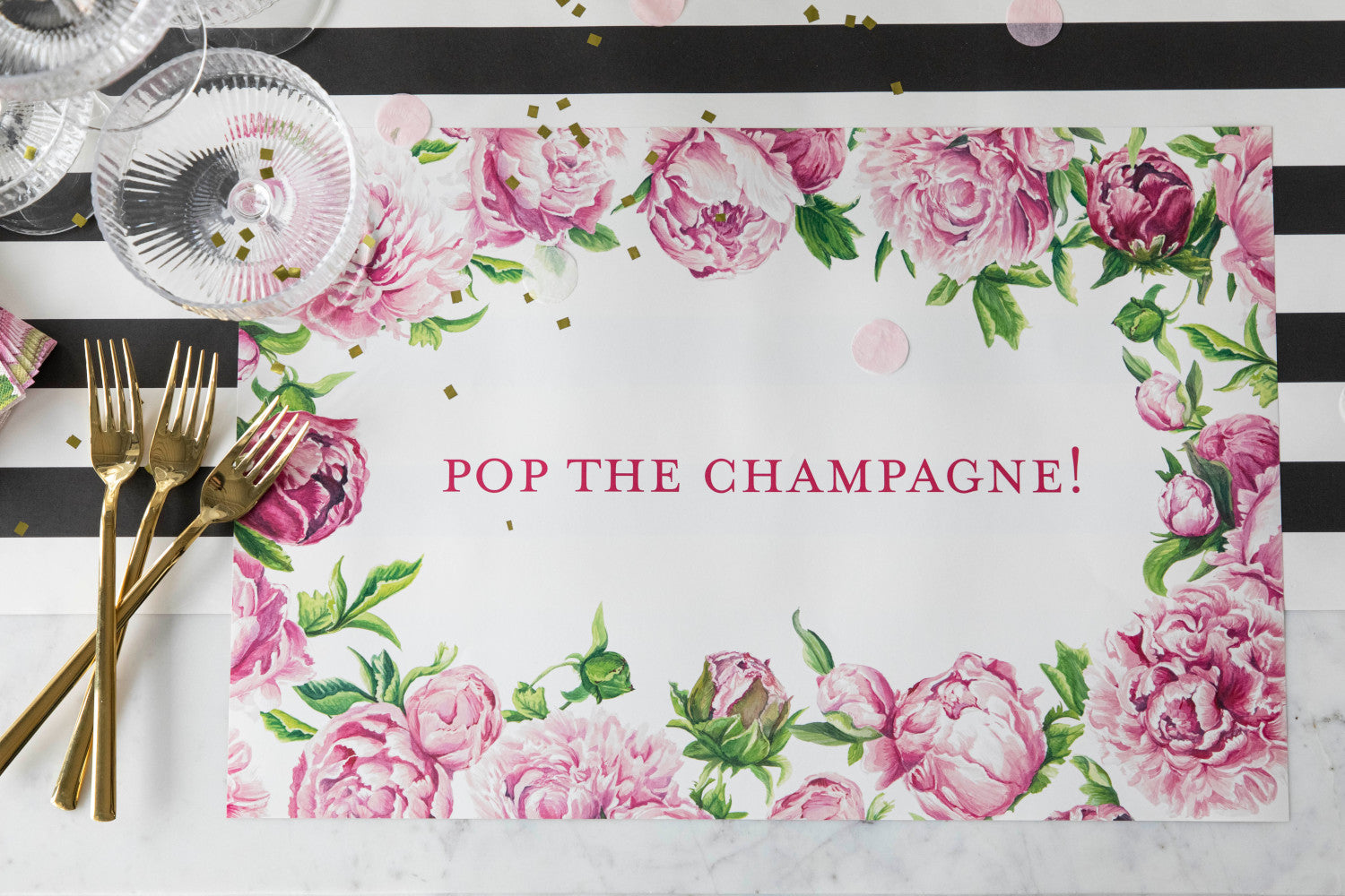 The Peony Personalized Placemat under a festive place setting, with "POP THE CHAMPAGNE!" printed in deep pink, from above.