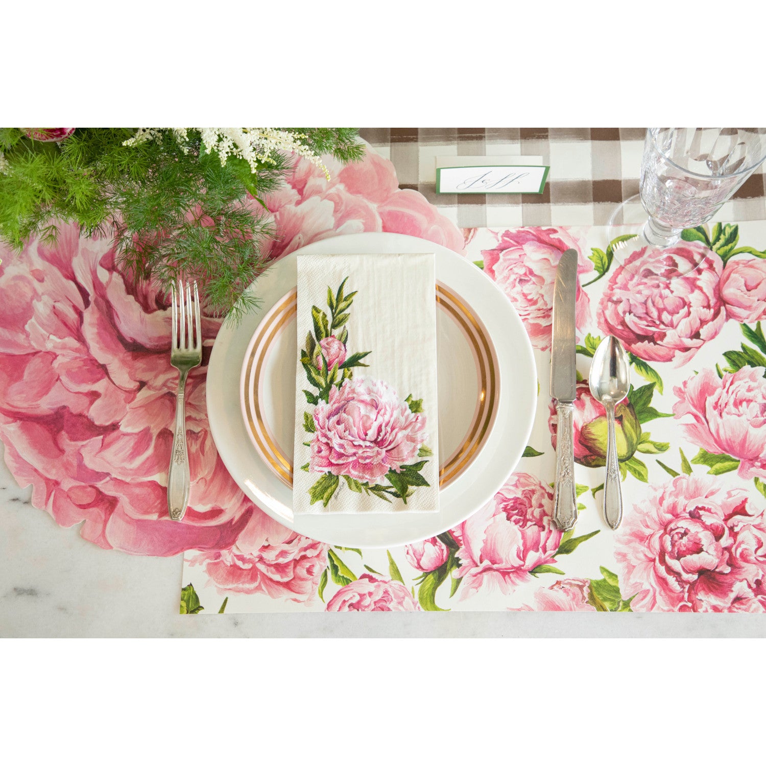 An elegant floral place setting featuring a Peony Guest Napkin centered on the plate, from above.