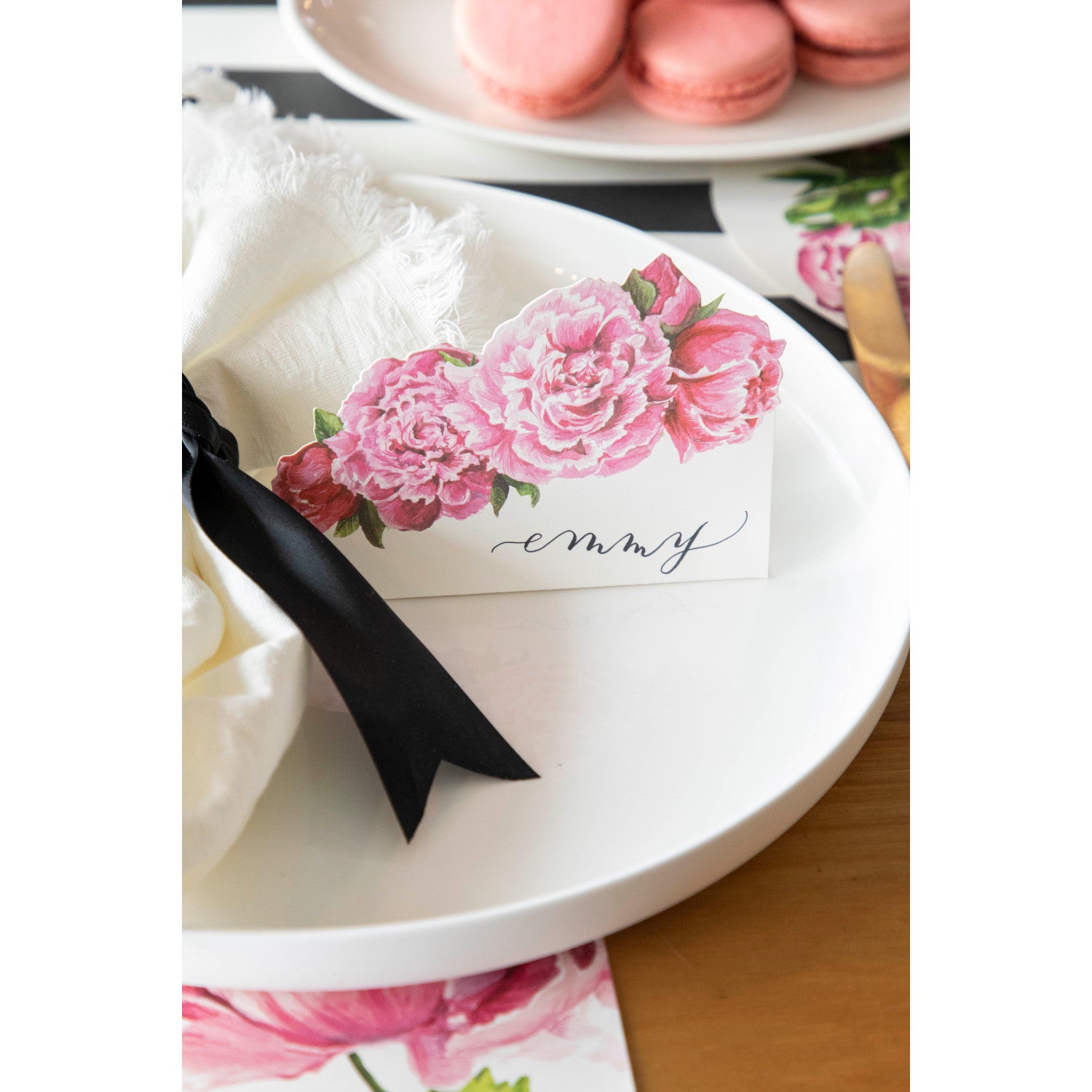 An elegant place setting featuring a Peony Place Card labeled "Emmy" standing on the plate.