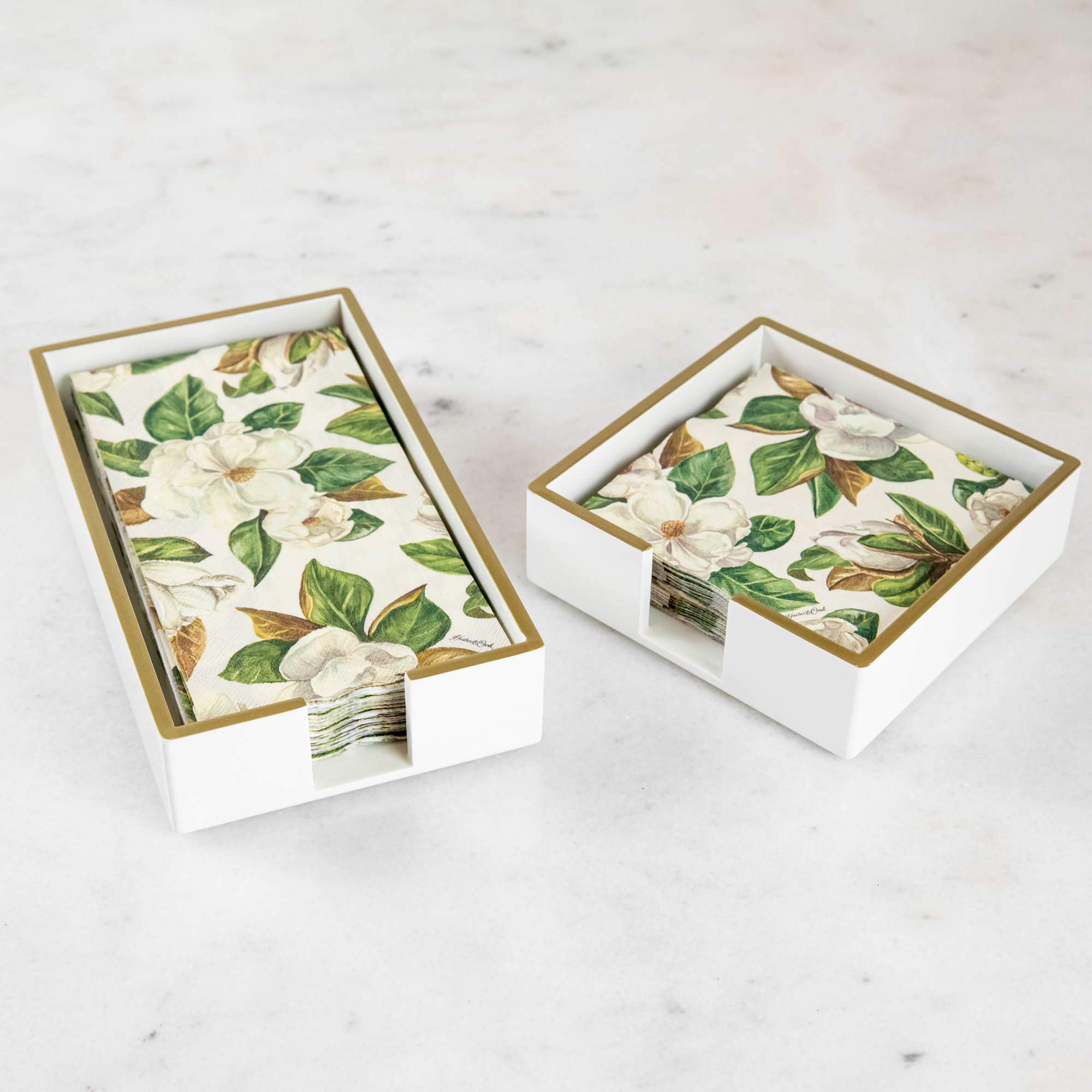 A lacquered wood holder for beverage and guest napkins, featuring a white color with gold trim and a floral pattern napkin inside.